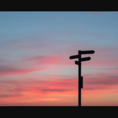 A traffic directional sign post against a sunset background.